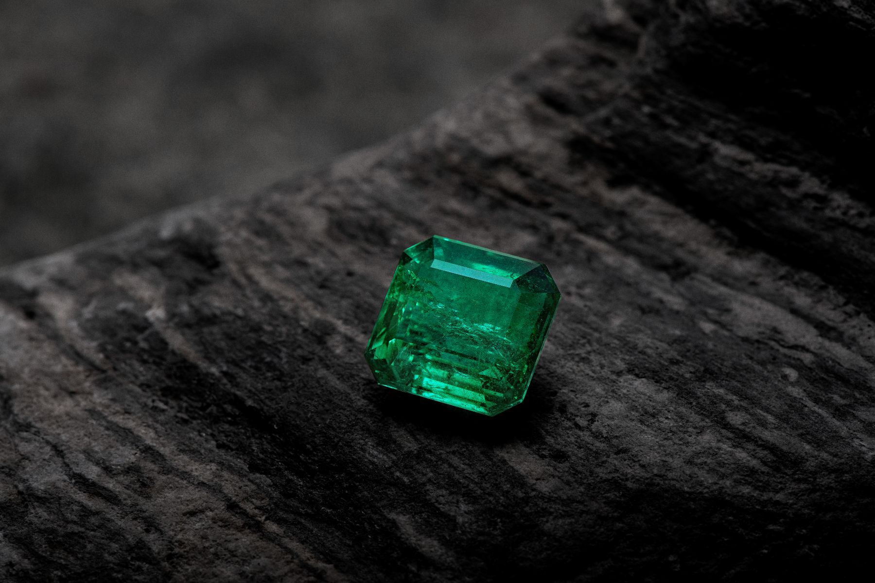 一顆哥倫比亞木佐祖母綠（Muzo Emerald）置於原岩之上，展現「Muzo Green」木佐綠的飽和色彩——產地是頂級彩色寶石價值的核心構成
