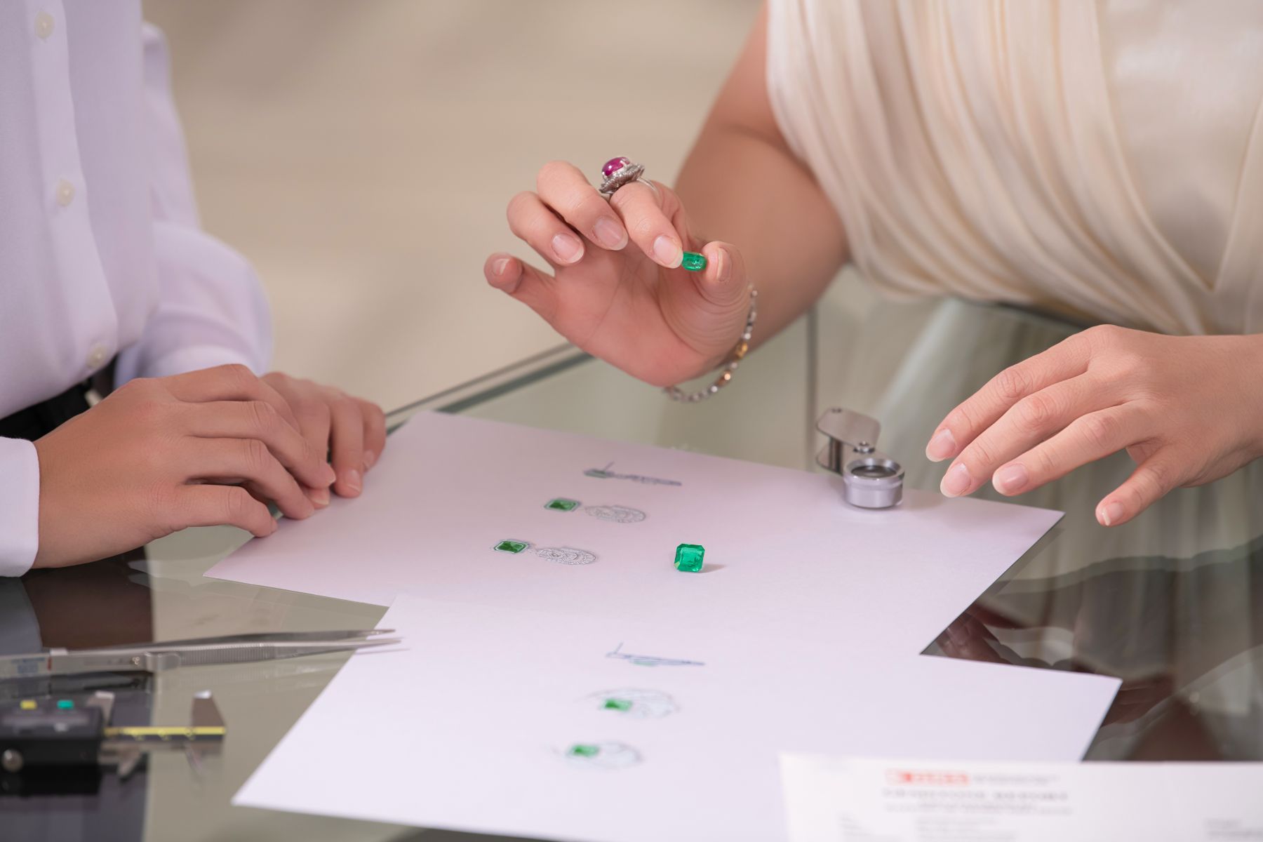 A JUSTLEE consultant reviews Colombian emeralds and a GRS gemstone report with a collector — auction-grade colored gemstones in private viewing