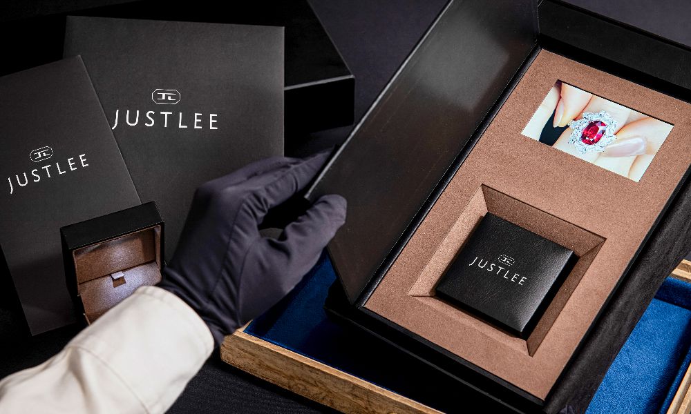 JUSTLEE Legacy Capsule open box — left compartment holds the bespoke jewelry piece with unheated certified gemstone; right compartment features an embedded video display screen. A single heirloom object integrating collector-grade rare gemstones and video memory, winner of the 21st National Brand Yushan Award Best Product category.