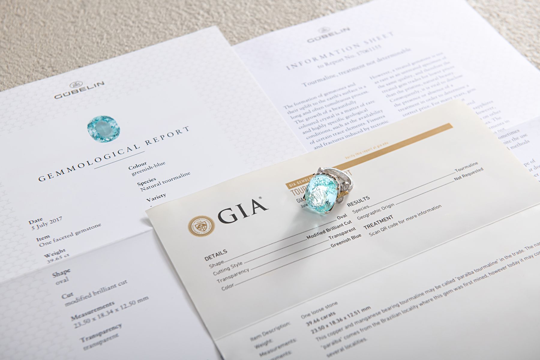 A Paraiba tourmaline loose stone resting on concurrent Gübelin and GIA gemmological reports — dual certification for collector-grade coloured gemstones