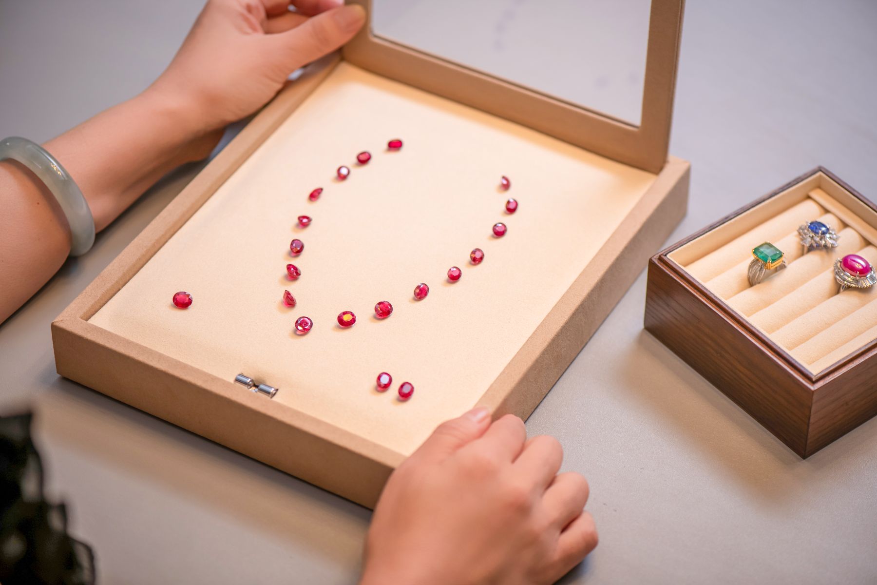 JUSTLEE private viewing: loose rubies arranged on a suede tray alongside sapphire, emerald, and ruby rings — a collector's selection across coloured stone varieties